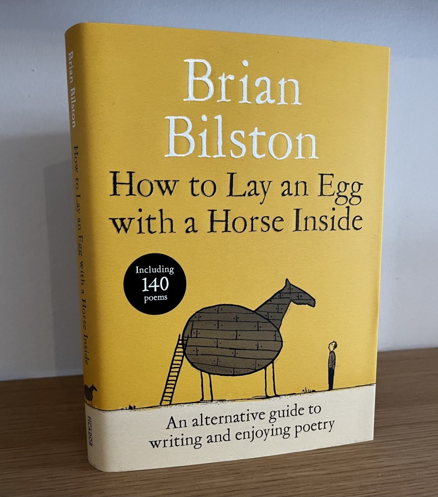 A photo of my new book ‘How to Lay an Egg with a Horse Inside’. It’s a beautiful hardback edition in gold / yellow colours featuring an illustration on the front of a man looking up at a wooden horse which has a body shaped like an egg.